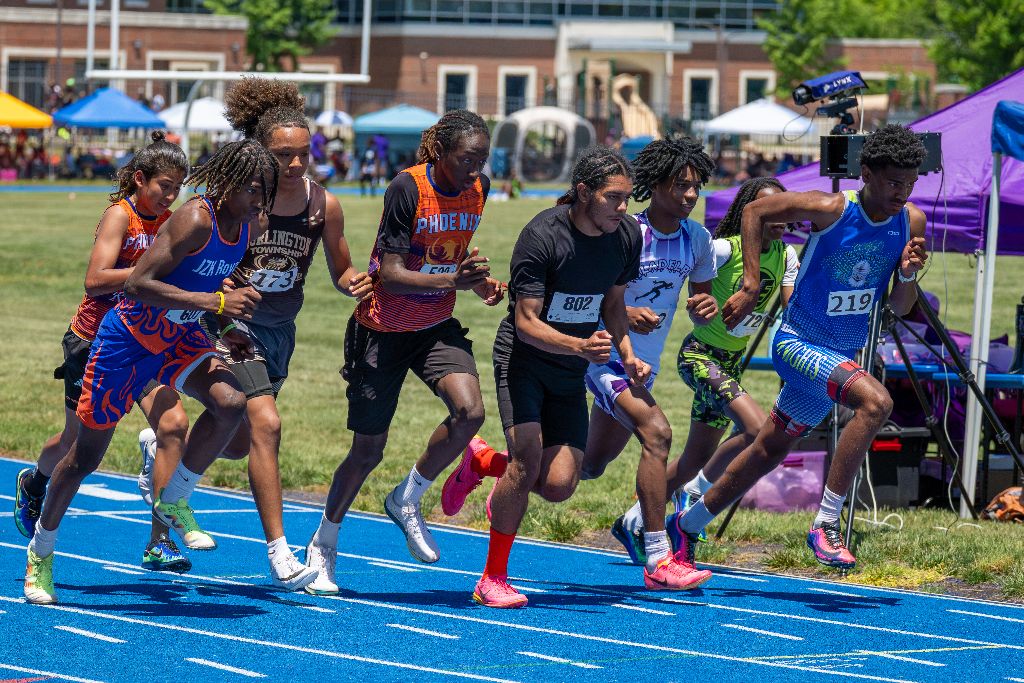 Youth athletes exploding out of the blocks at the start of a race on a blue track